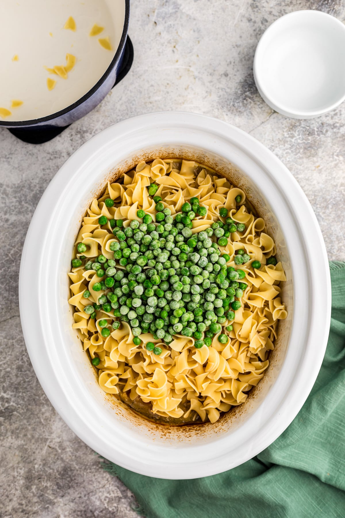 egg noodles, peas on top of chicken and sauce in a slow cooker.