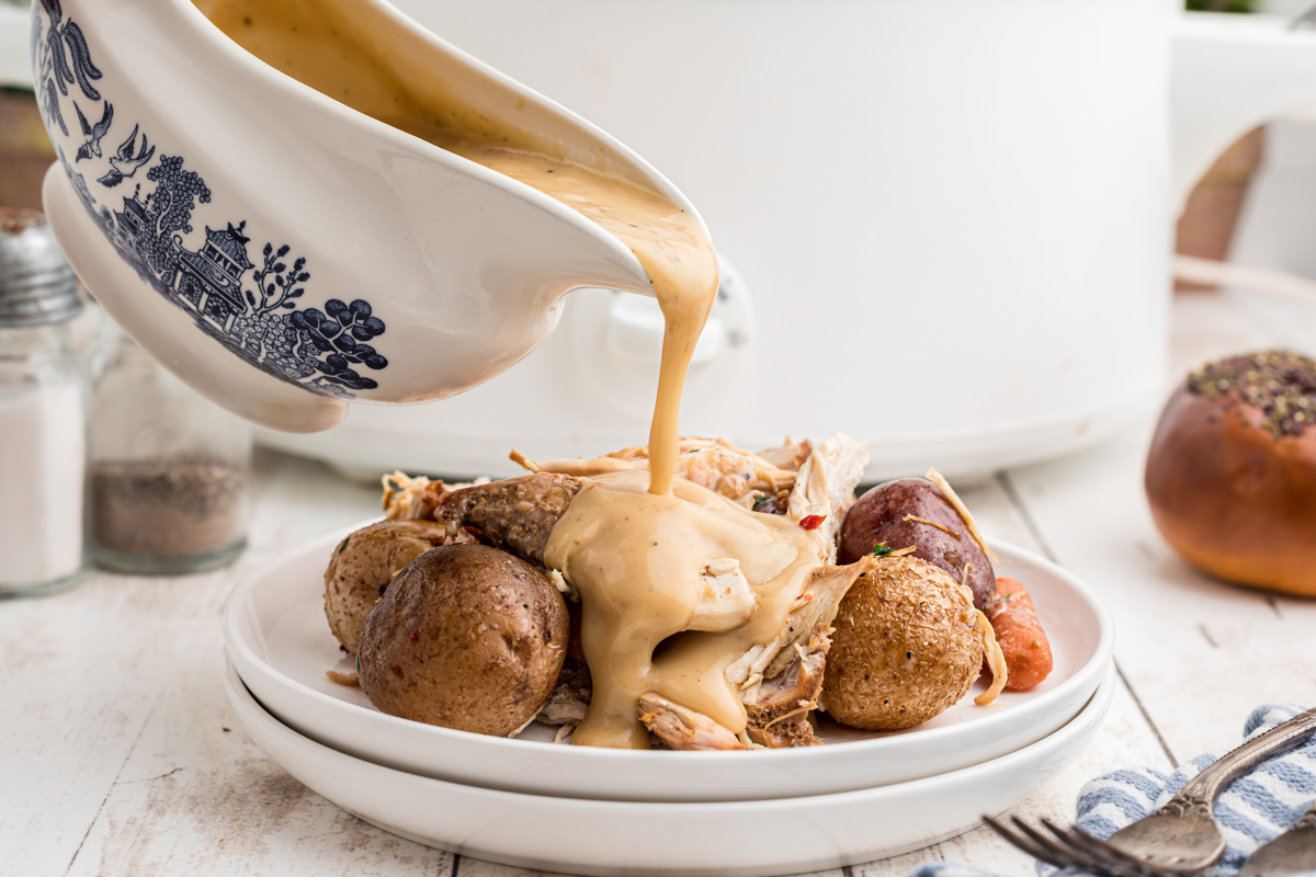 Creamy gravy being poured over  chicken, carrots and potatoes.