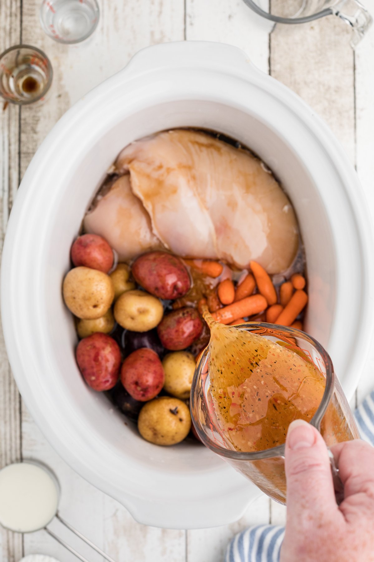Italian dressing being poured over chicken and vegetables in crockpot.