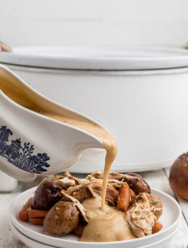 Gravy being pour over italian chicken on a white plate.