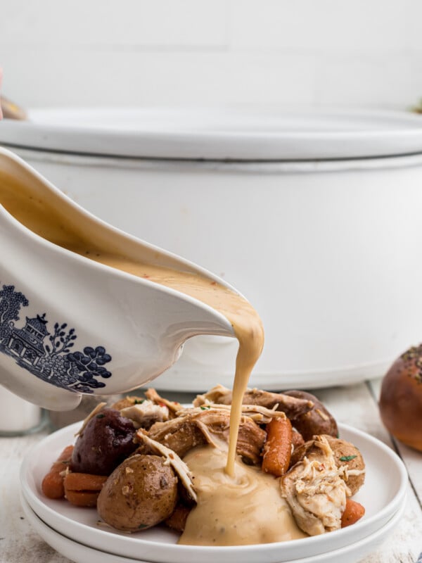 Gravy being pour over italian chicken on a white plate.