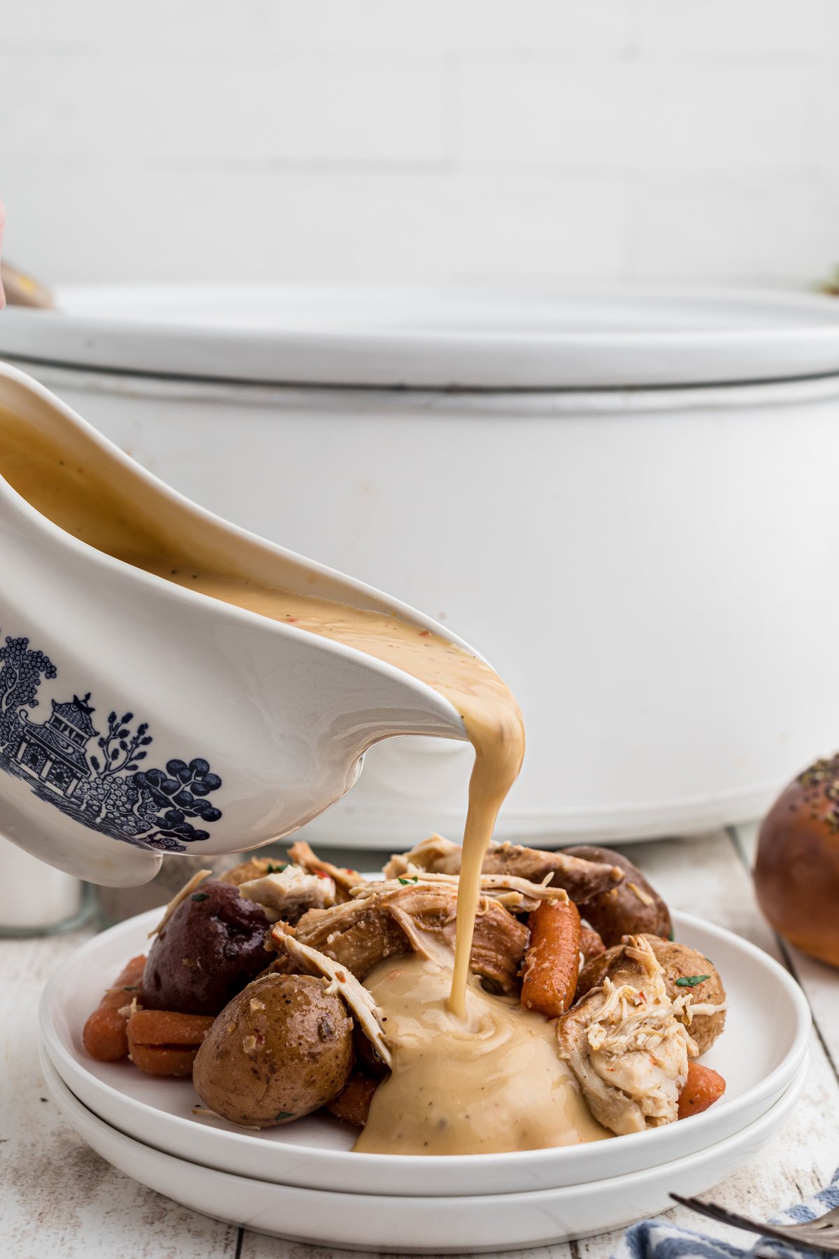 Gravy being pour over italian chicken on a white plate.