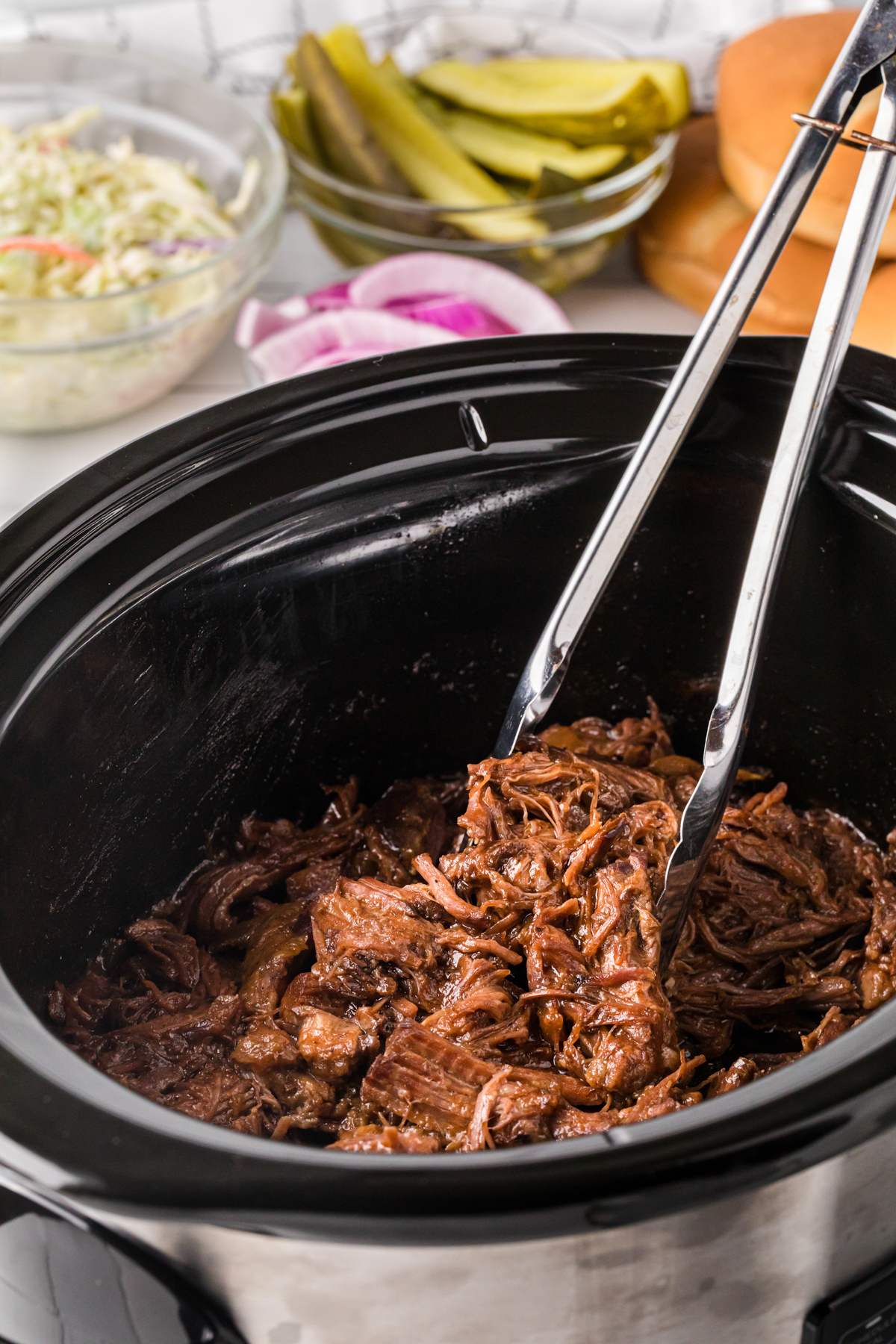 BBQ beef in tongs in a crockpot.