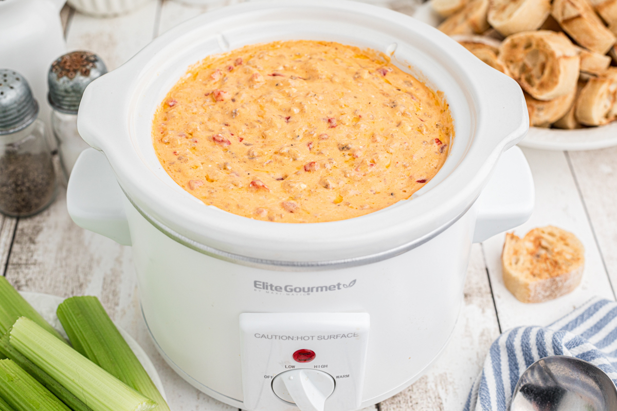 Warm dip in a white slow cooker with celery and bread on the side.