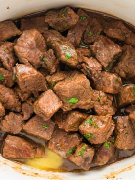 Steak bites in a slow cooker with parsley on it.