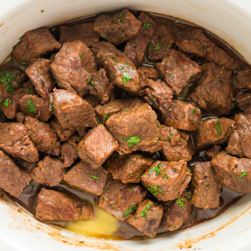 Steak bites in a slow cooker with parsley on it.
