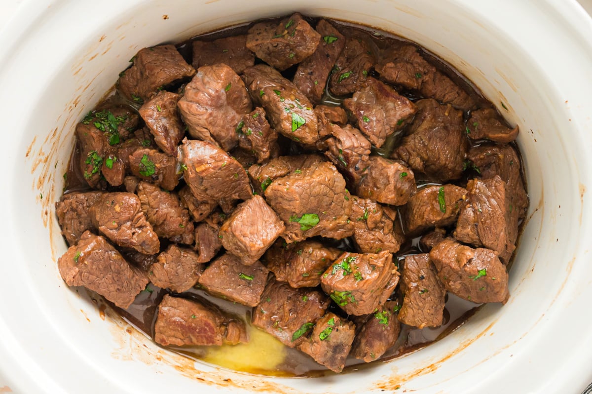 Steak bites in a slow cooker with parsley on it.