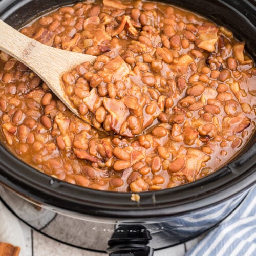 baked beans in a slow cooker with a wooden spoon in them.