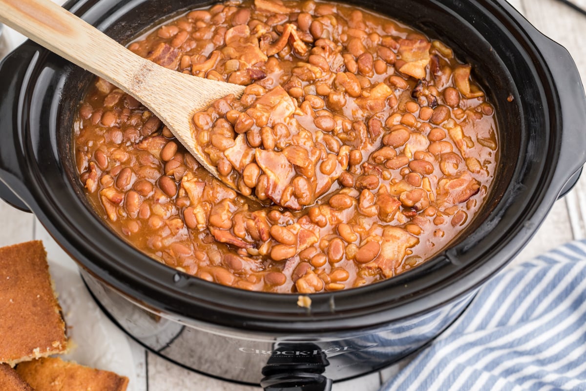 baked beans in a slow cooker with a wooden spoon in them.