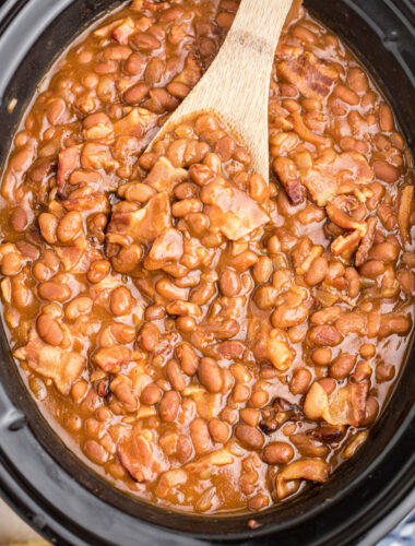 Baked beans in a slow cooekr with a spoon in them.