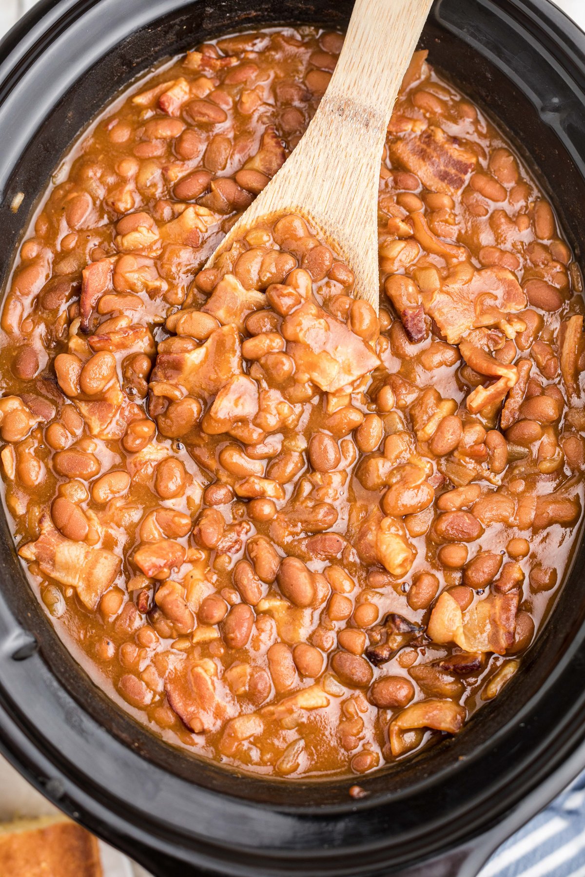 Baked beans in a slow cooekr with a spoon in them.