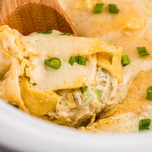 Chicken enchiladas casserole with green sauce and sour cream in a slow cooker.