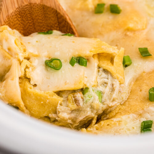 Chicken enchiladas casserole with green sauce and sour cream in a slow cooker.