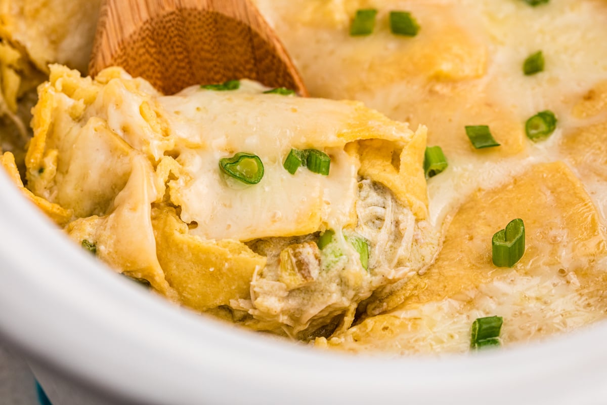 Chicken enchiladas casserole with green sauce and sour cream in a slow cooker.