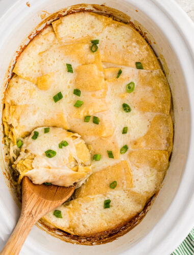 Sour cream enchilada casserole with a wooden spoon in it.