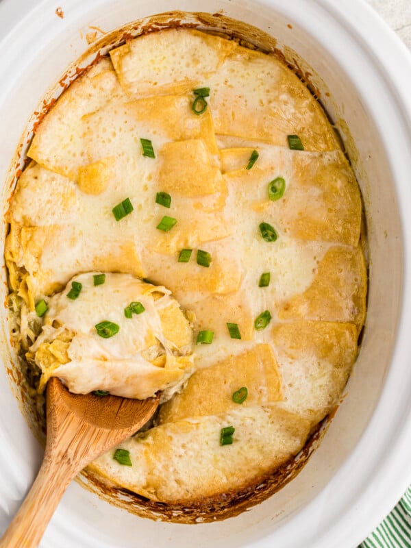 Sour cream enchilada casserole with a wooden spoon in it.