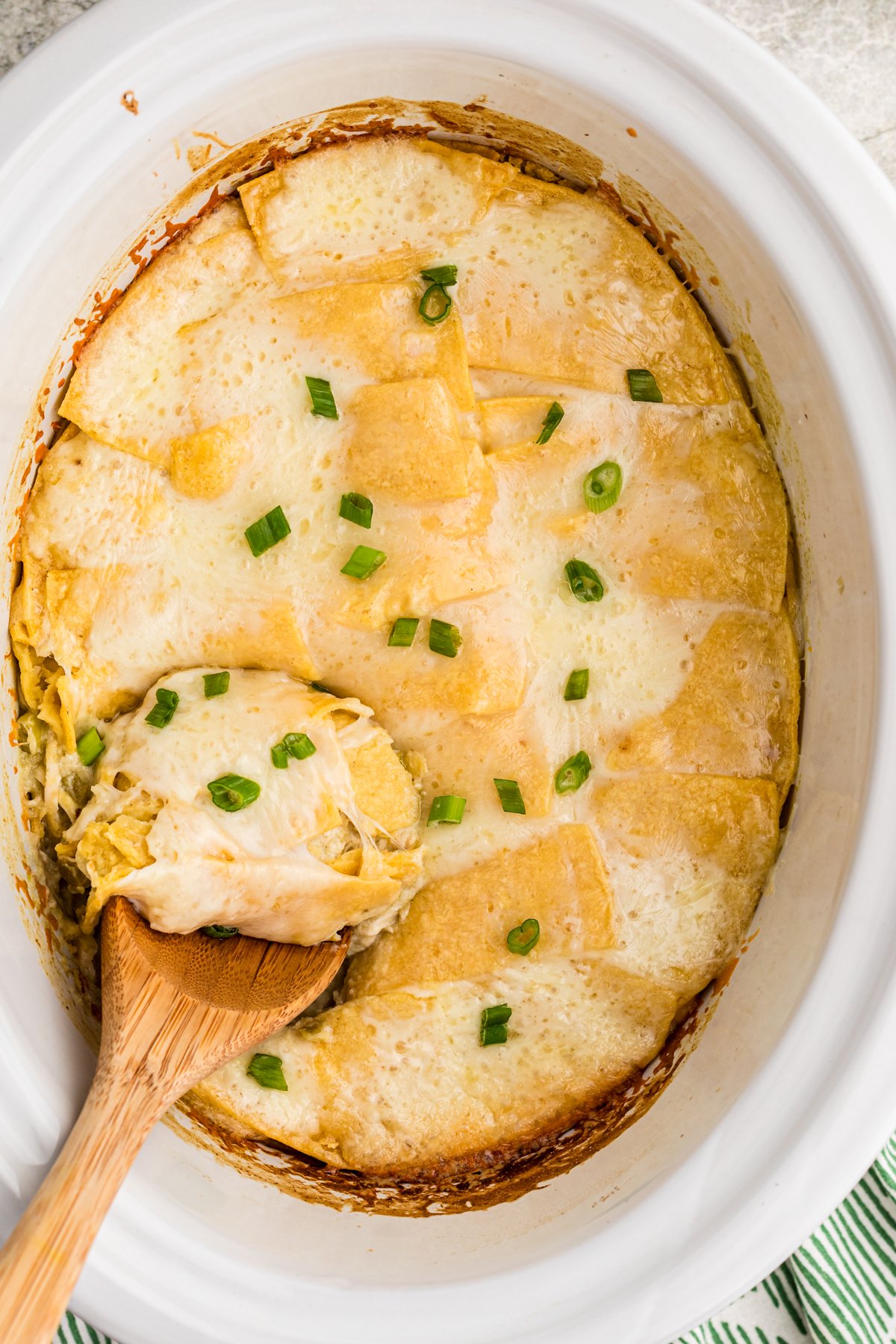 Sour cream enchilada casserole with a wooden spoon in it.