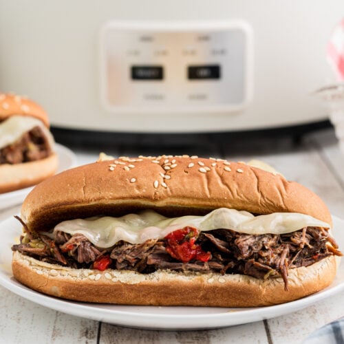 2 Italian beef sandwiches in front of a slow cooker.