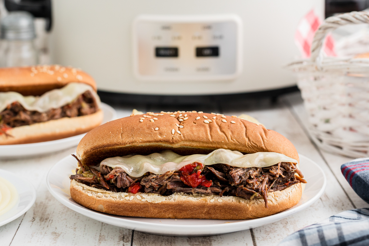 2 Italian beef sandwiches in front of a slow cooker.