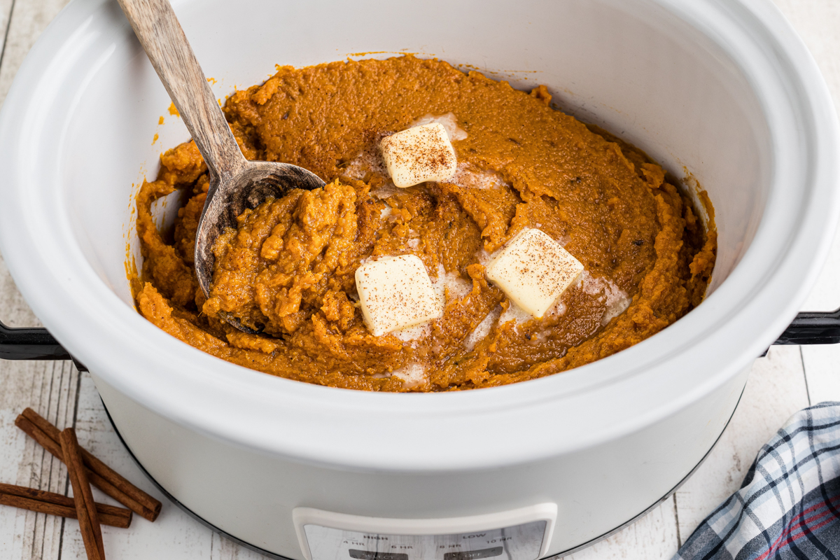 Mashed sweet potatoes with a wooden spoon in them.