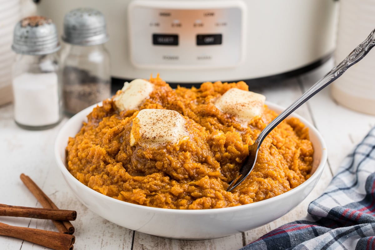 Bowl of mashed sweet potatoes with butter pats on top.