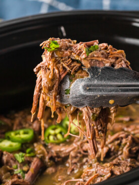tongs pulling out some of the cooked meat from the crockpot.