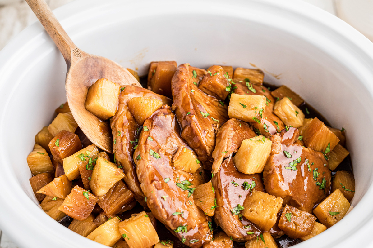 cooked pork chops in a crokcpot with a wooden spoon in them.