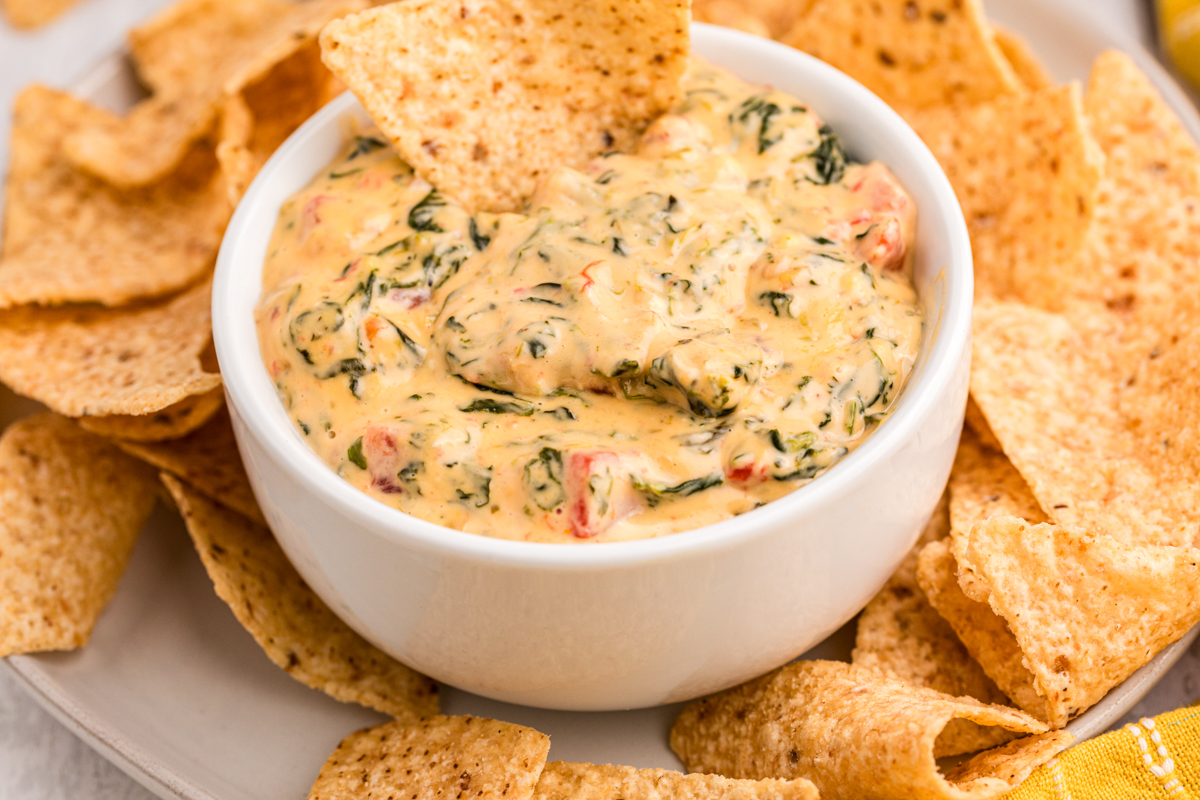 bowl of spinach queso dip with chip in it.