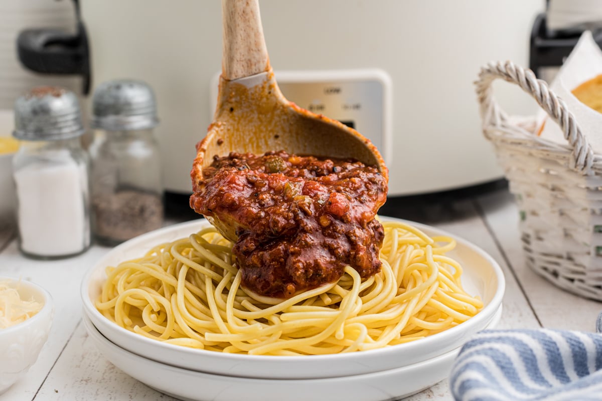 spaghetti sauce over noodles on a plate in front of a slow cooker.