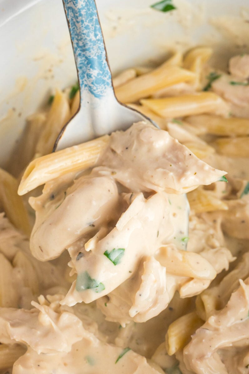 chicken alfredo on a metal spoon coming from a slow cooker.