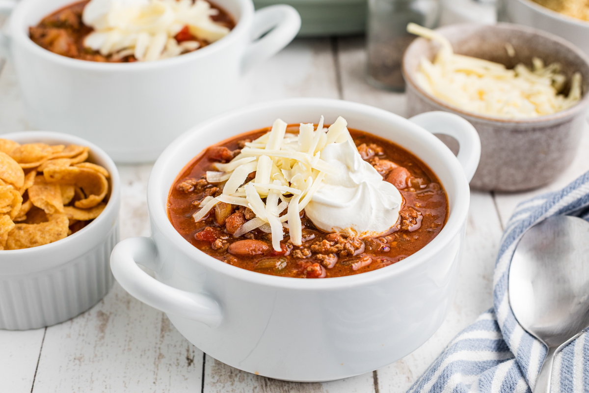 chili in a white bowl with sour cream and cheese. Fritos in the background.