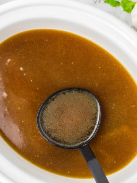Chicken stock in a slow cooker in a ladle.
