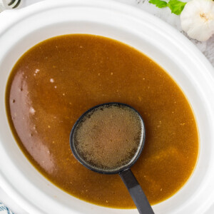 Chicken stock in a slow cooker in a ladle.