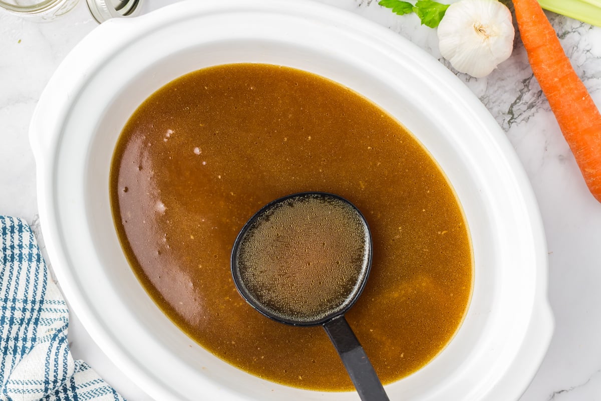 Chicken stock in a slow cooker in a ladle.