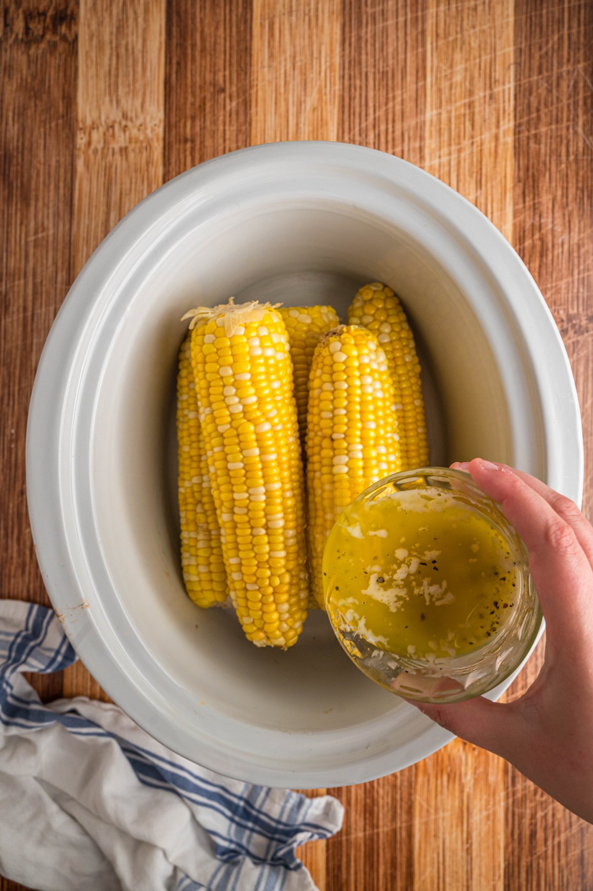 butter mixture being poured over corn in a slow cooker.
