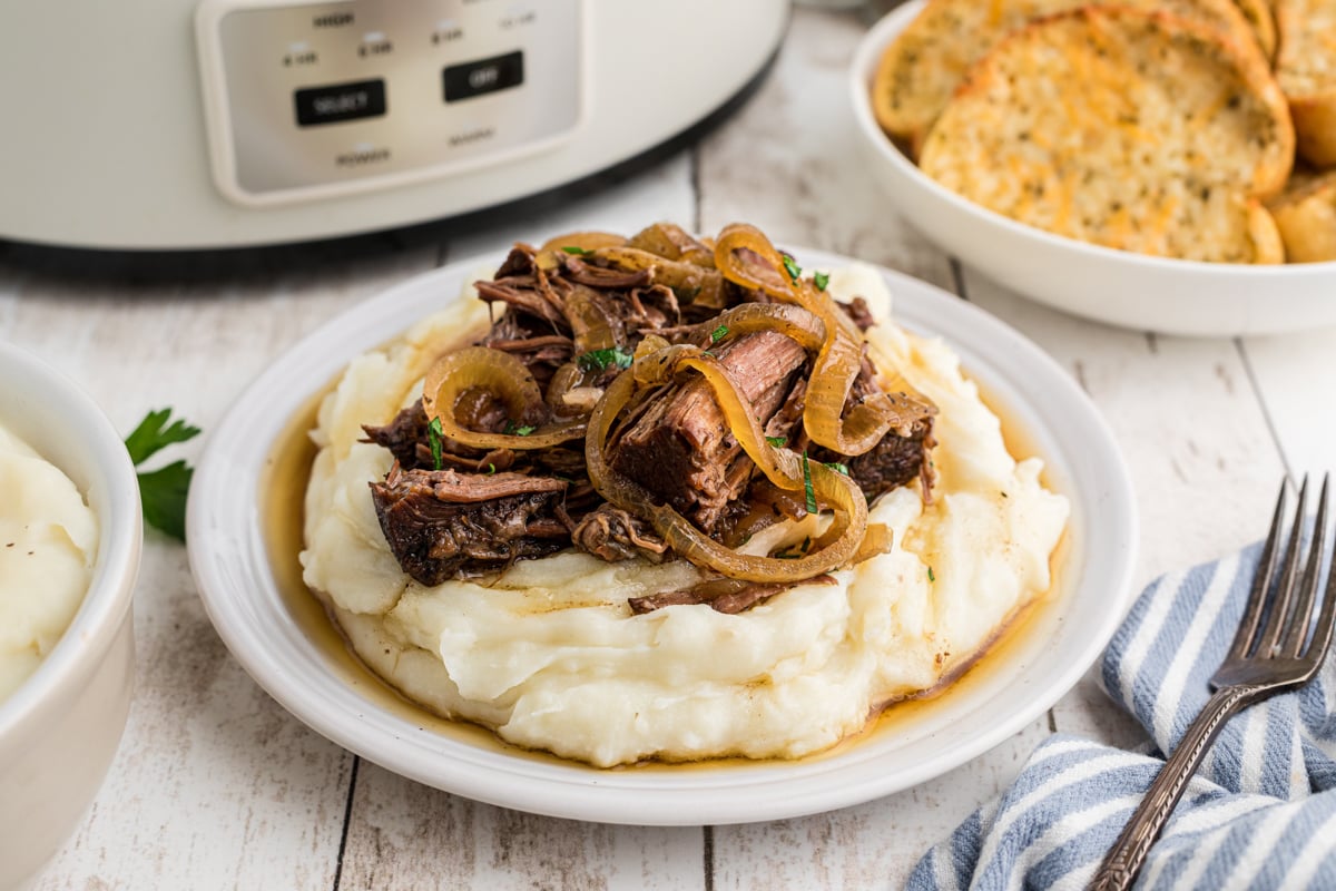 crockpot french onion pot roast over mashed potatoes on a white plate.