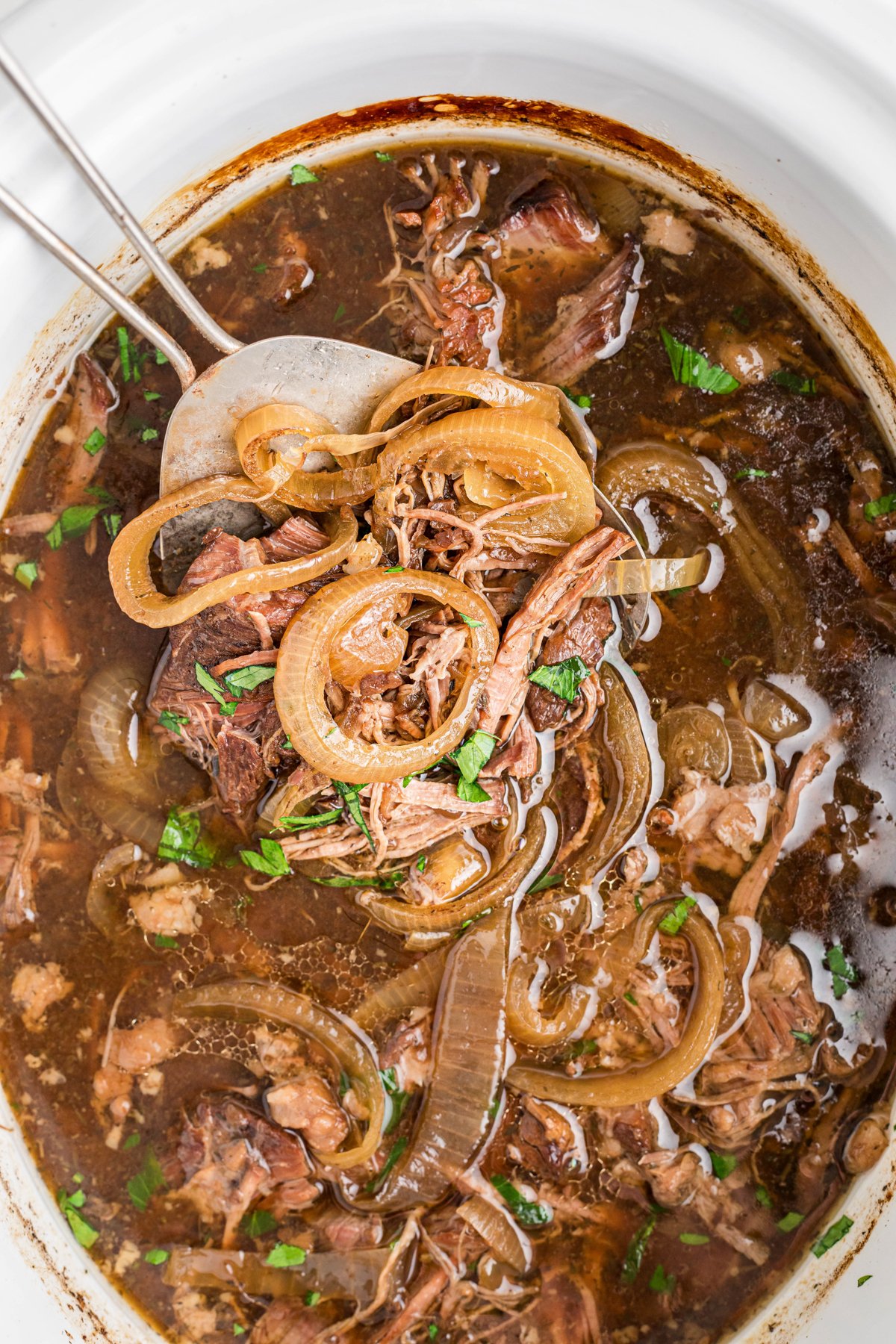 scooping out slow cooker french onion pot roast with a spatula.