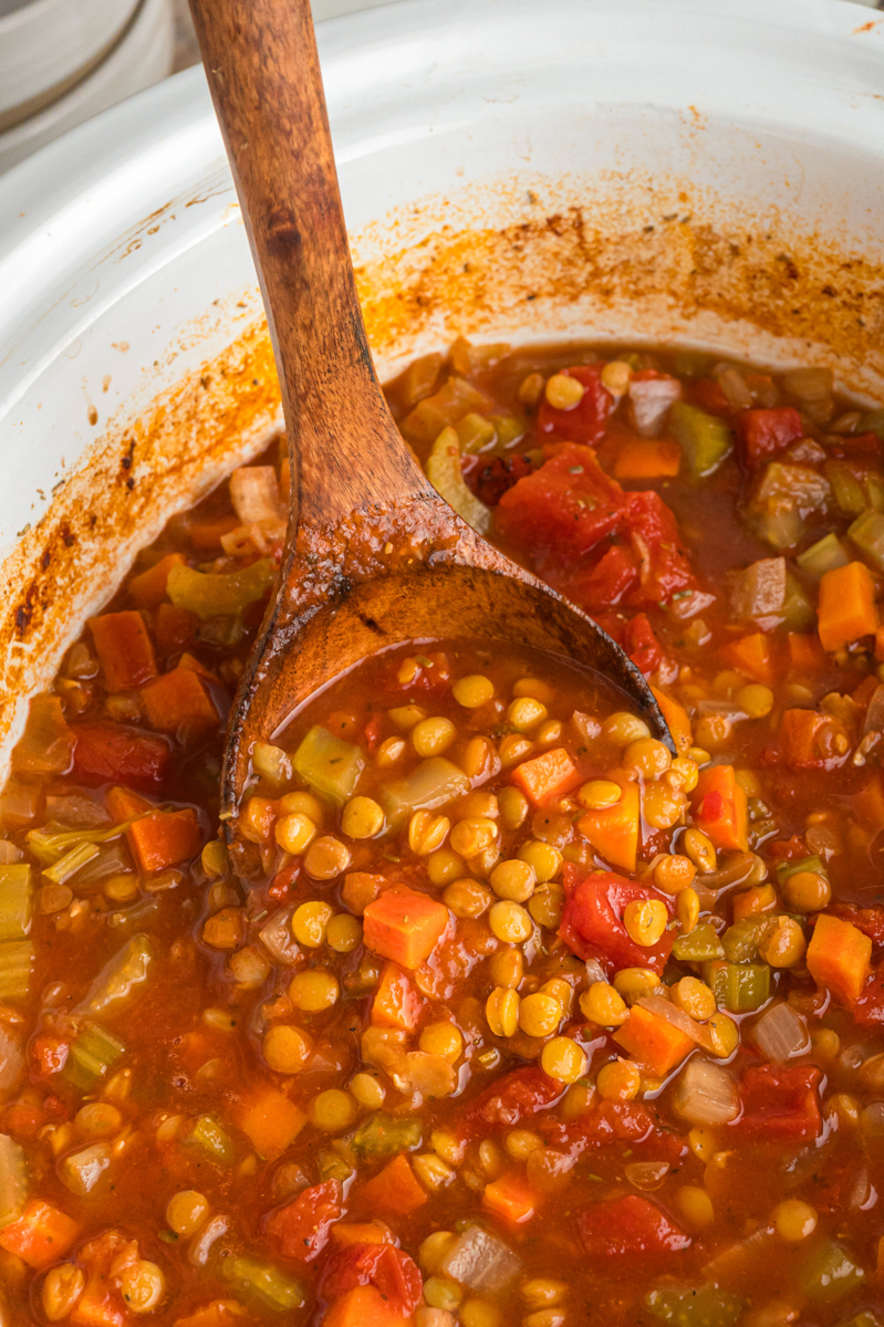 Lentil soup in a slow cooker and a wooden spoon.