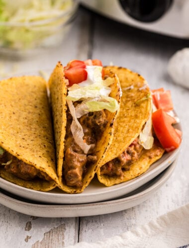 3 taco on a plate in front of a slow cooker.