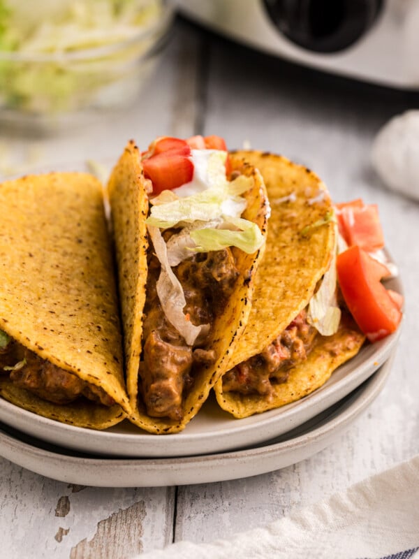 3 taco on a plate in front of a slow cooker.