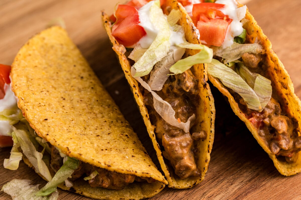 tacos on a cutting bord with lettuce and tomatoes.