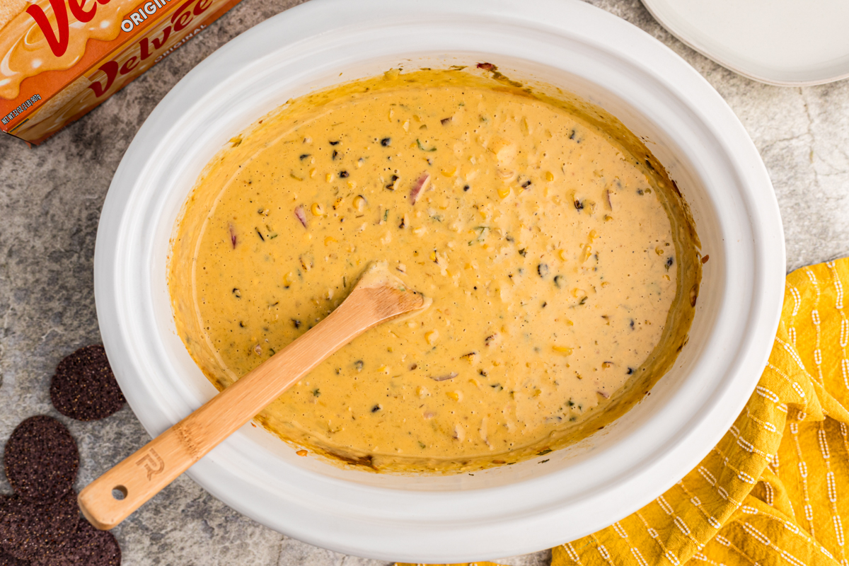 Overhead shot of corn dip with wooden spoon in it.