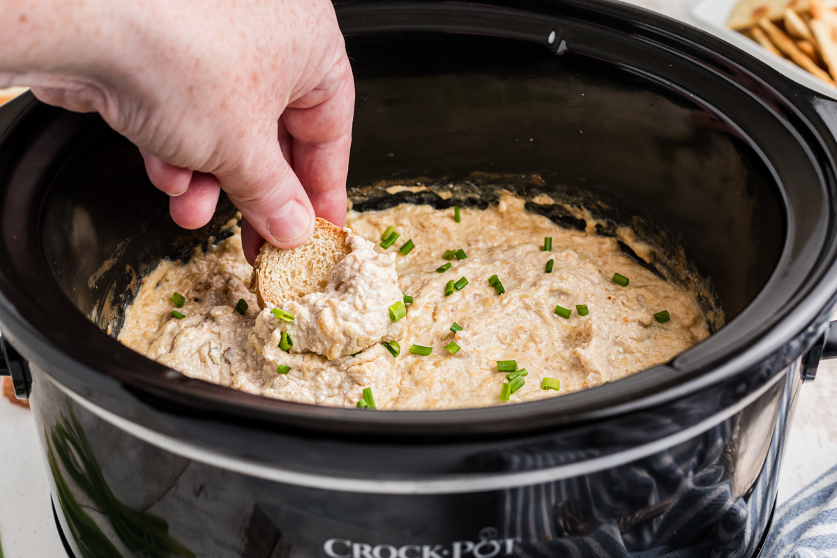 Dip in a crockpot with bread being dipped in, chives on top.