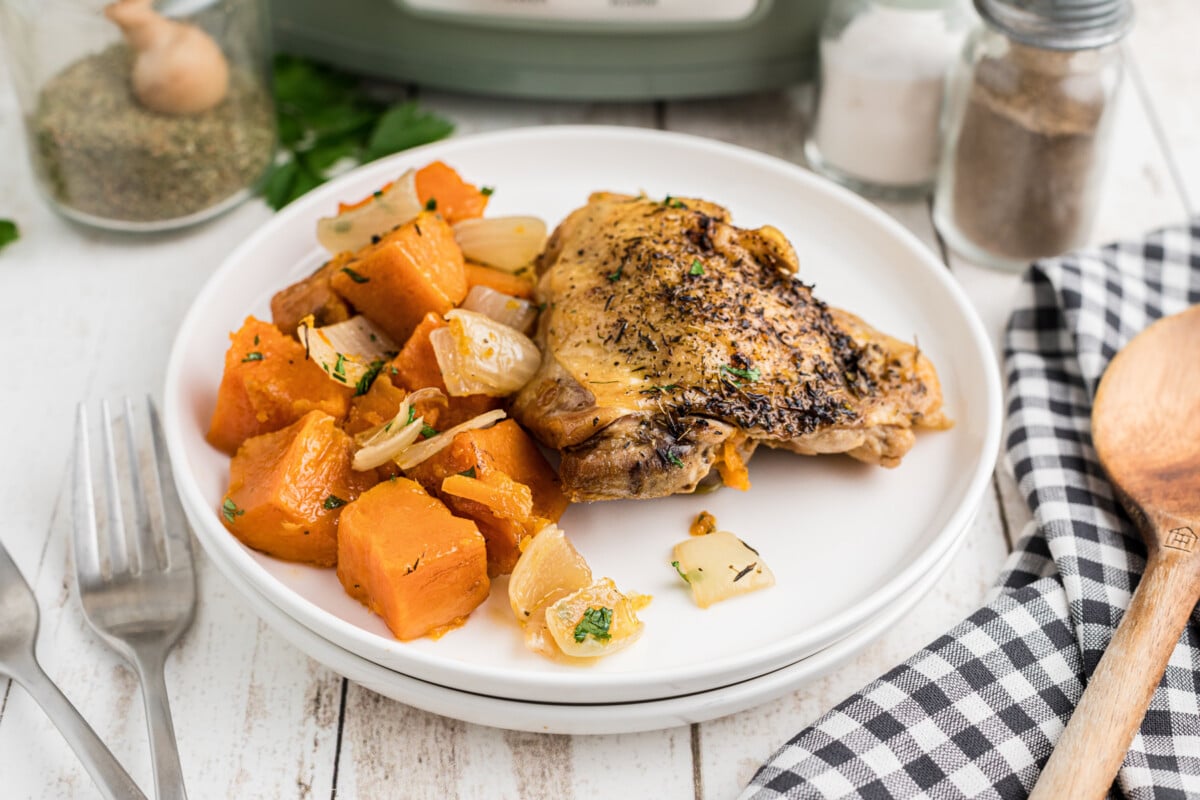 a chicken thigh with sweet potatoes on a white plate.
