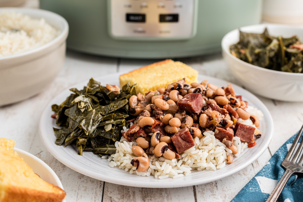 Plate of black eyed peas on rice with collard greens and cornbread.