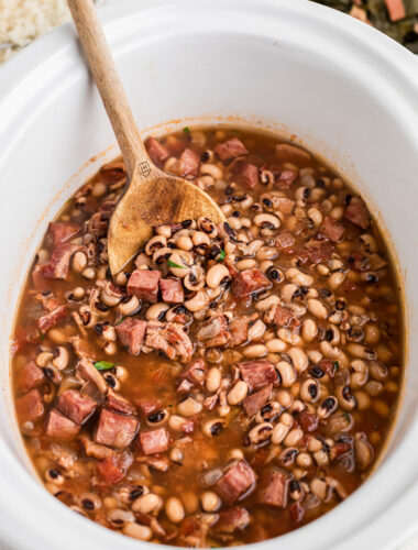 Black eyed peas in a white slow cooker with a wooden spoon in it.