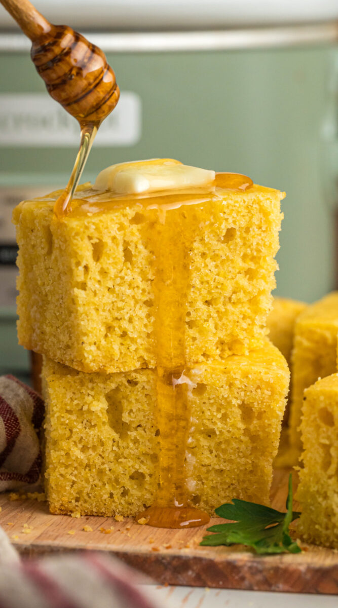 2 pieces of stacked cornbread with honey being drizzeled over.