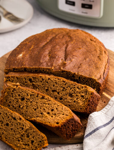 Pumpkin bread on a cutting board in front of a slow cooker.