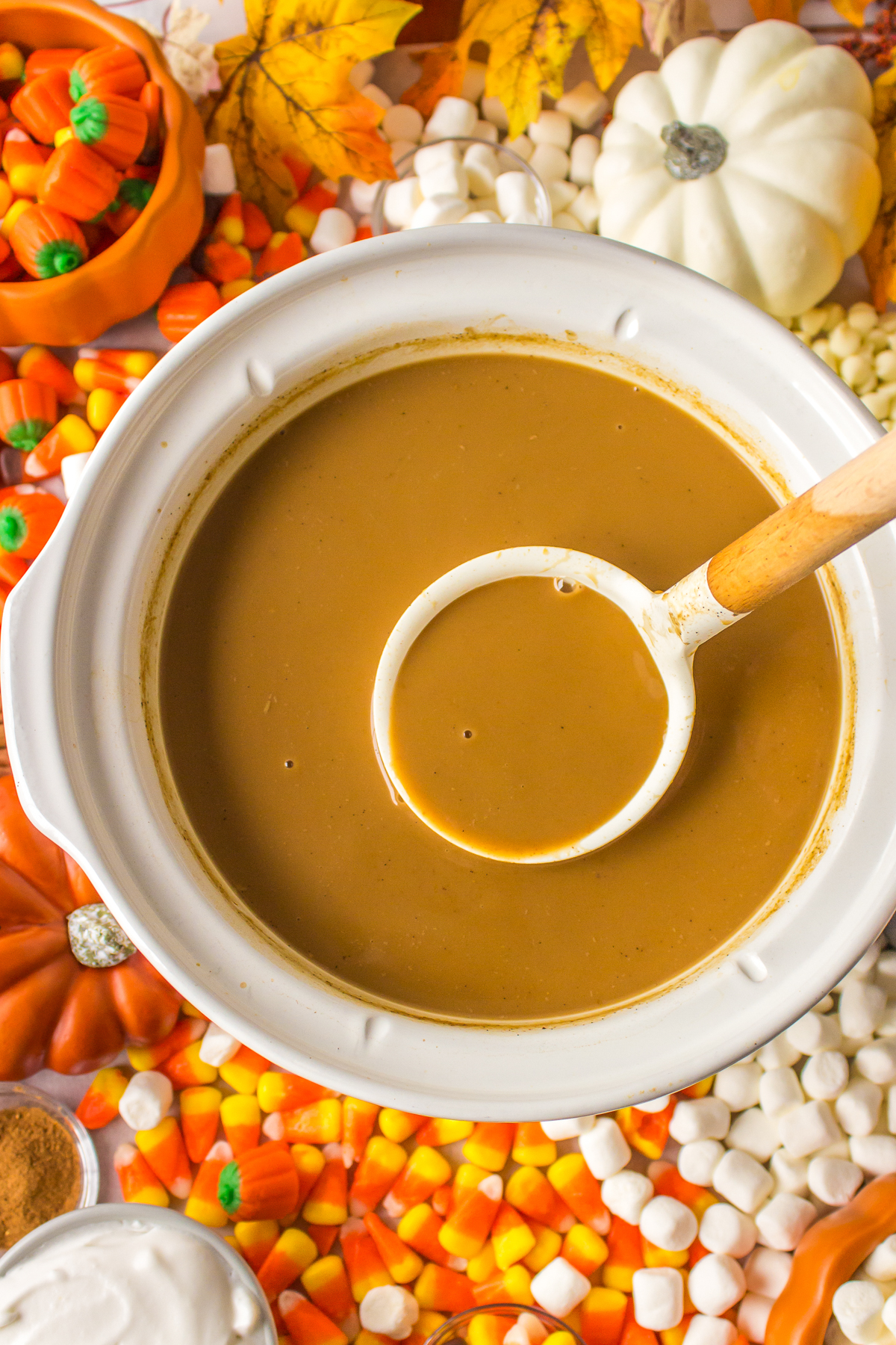 pumpkin spice lattes in a slow cooker with a ladle.