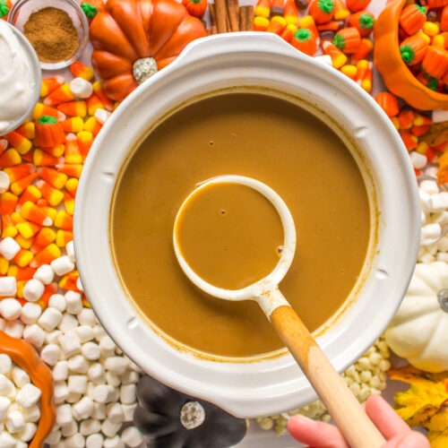 overhead shot of pumpkin spice lattes in a slow cooker with candies around it.